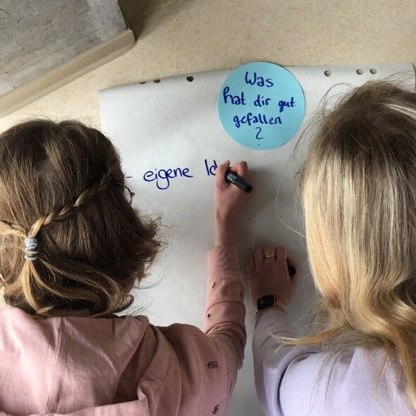 Zwei Jugendliche schreiben auf ein großes Papier unter die Überschrift Was hat dir gut gefallen?