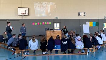 In einer Turnhalle sitzen viele Schüler*innen im Kreis. Leonie Bröcheler hält einen Workshop.