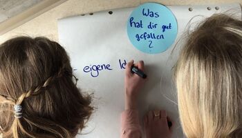 Zwei Jugendliche schreiben auf ein großes Papier unter die Überschrift Was hat dir gut gefallen?