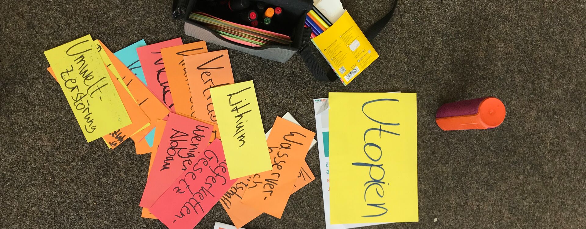 Auf dem Boden liegen viele Moderationskarten aus einem Workshop. Die Begriffe Utopien, Lithium, Lieferkettengesetz, weniger Abbau und Umweltzerstörung sind zu lesen.