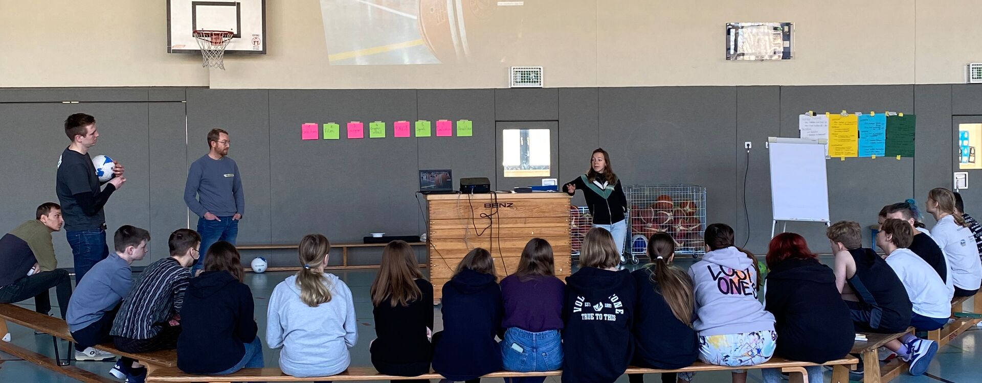 In einer Turnhalle sitzen viele Schüler*innen im Kreis. Leonie Bröcheler hält einen Workshop.
