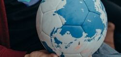 Ein fair produzierter Lederball wird von einer Multiplikatorin gehalten