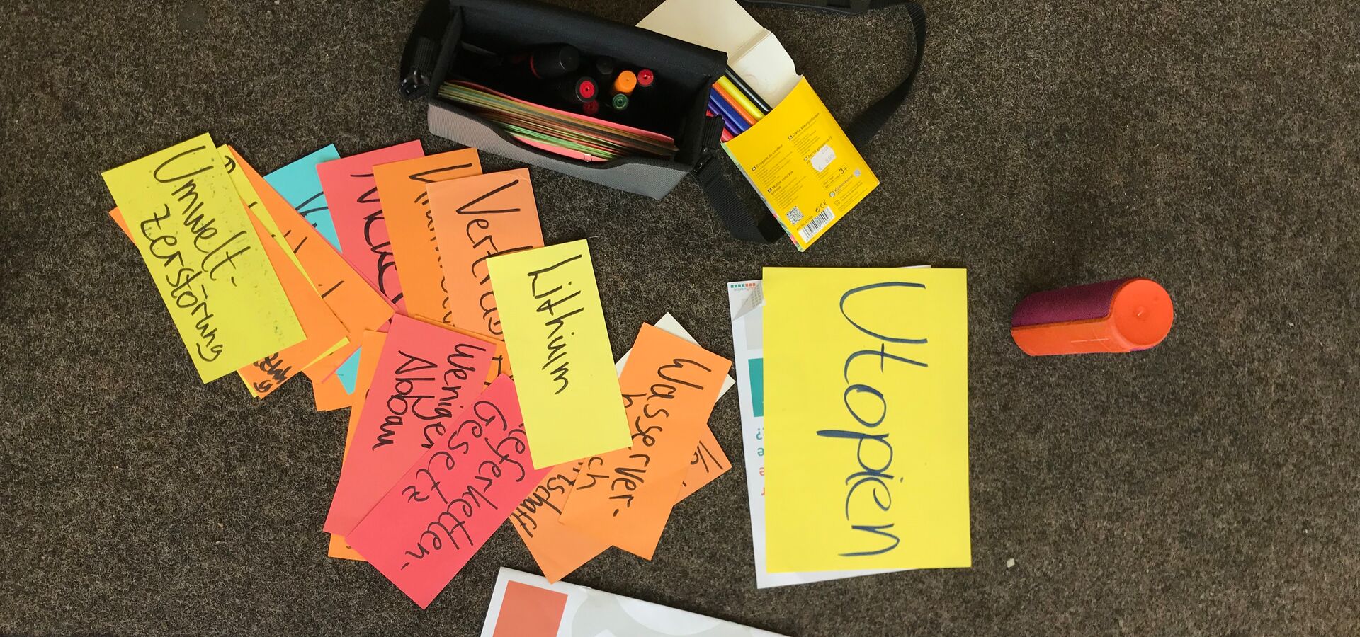 IMG_8283.jpg Auf dem Boden liegen viele Moderationskarten aus einem Workshop. Die Begriffe Utopien, Lithium, Lieferkettengesetz, weniger Abbau und Umweltzerstörung sind zu lesen.
